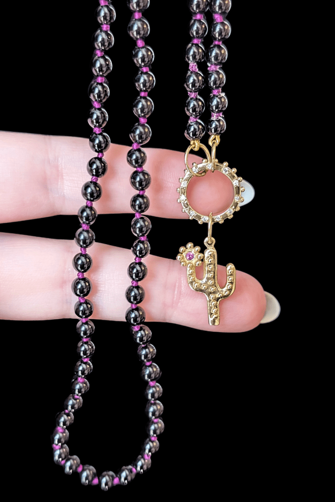Delphine Leymarie Onyx bead strand on purple silk with pink sapphire cactus charm from Beaumont Jewelry Collective.