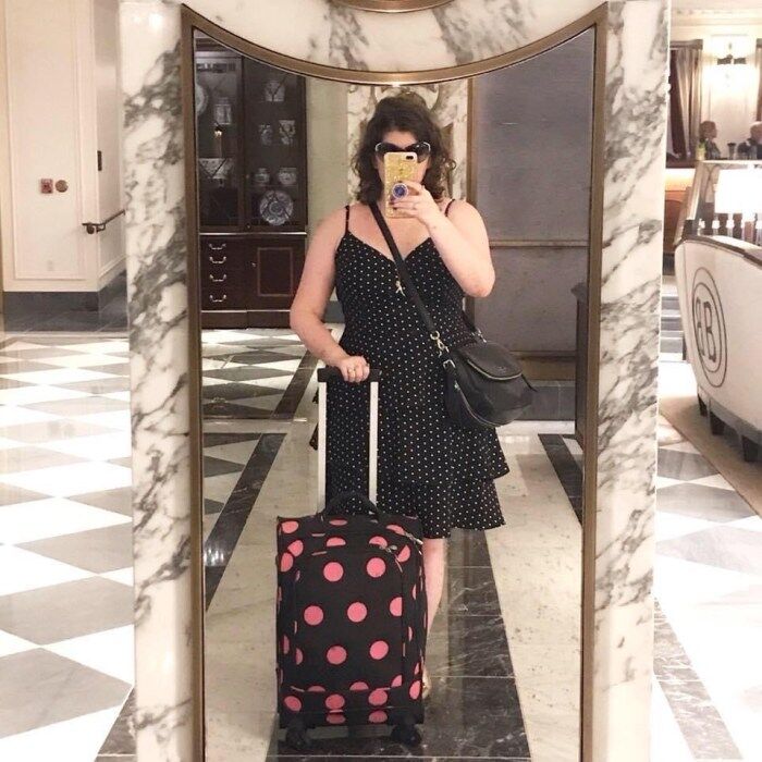 How to travel with jewelry! Me in a polka dot dress posing with a polka dot suitcase at the Waldorf Astoria Hotel in NYC